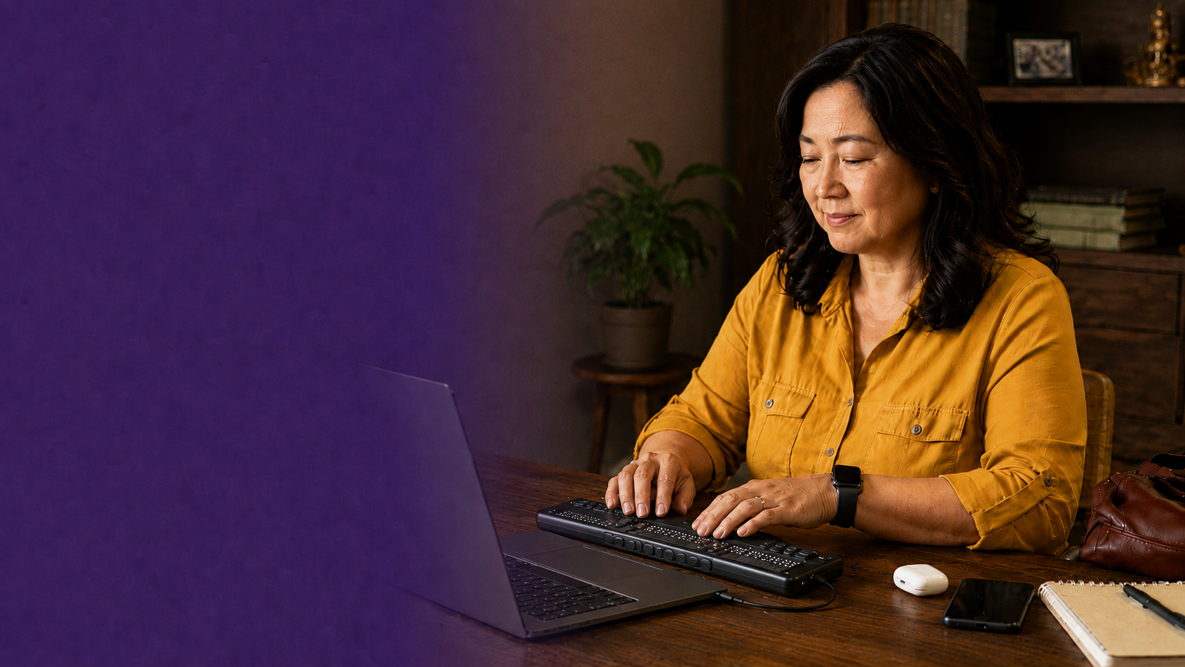 A woman reading with her fingers on a refreshable braille display connected to her laptop.