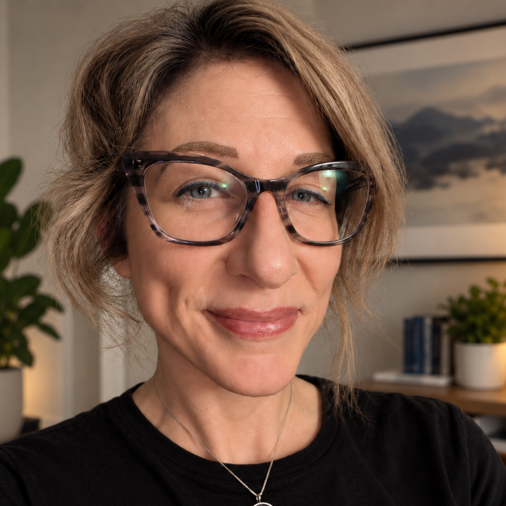 Close-up portrait of Kristen smiling, wearing cat-eye glasses and a black top.